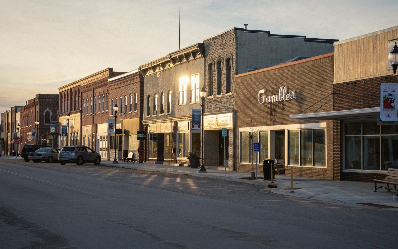 Empty small-town main street with brick storefronts lit by low sun, including the Gambles building
